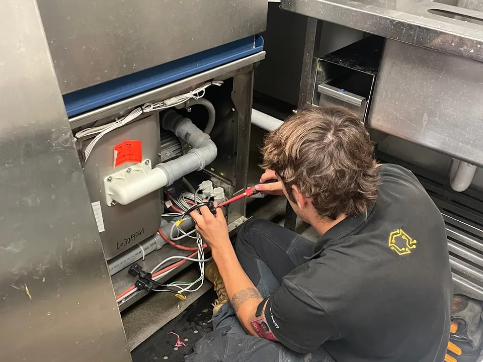 Commercial dishwasher repair Perth: Electeq technician testing the wiring under an undercounter dishwasher