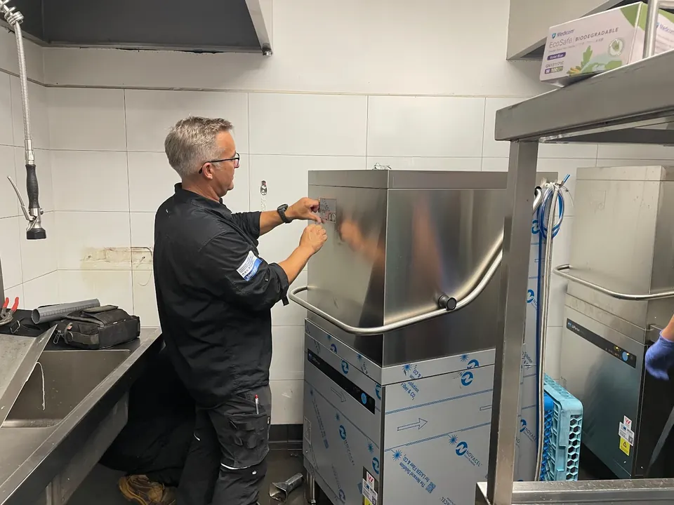 Commercial dishwasher repairs Perth: Electeq technician working on a pass-through dishwasher in a commercial kitchen